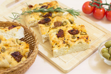 Freshly baked traditional Italian focaccia bread with green olives and sun-dried tomatoes, selective focus