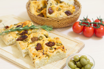 Freshly baked traditional Italian focaccia bread with green olives and sun-dried tomatoes, selective focus