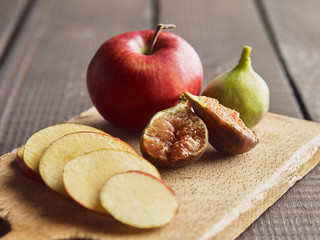 Red apple, green and black fig served on rustic wooden board