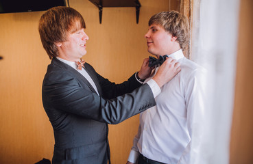 Groom and his friends prepare for the wedding. Grooms man helps the groom to put on black cufflinks on white sleeve of the shirt. Details of the morning of the wedding day