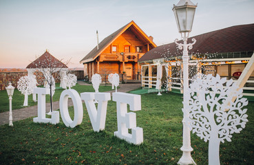 Love word outdoors. Big white plastic letters on the grass near flowers in the garden, wedding ceremony decoration, romantic holiday decor.