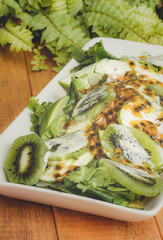 Mixed fresh salad leaves and fruit with passion fruit cream on wooden background.