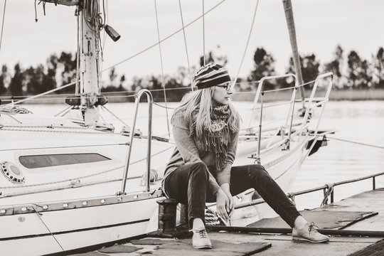 Cute blonde sitting in front of yacht. Monochrome image.