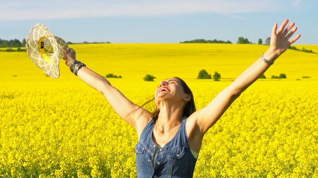Cheerful woman standing on rapseed's field, steadycam shot, slow motion shot at 240fps 
