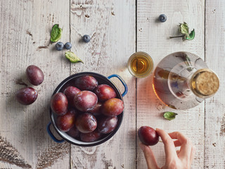 Plums and plum brandy on wooden white table. Hand takes a plum.