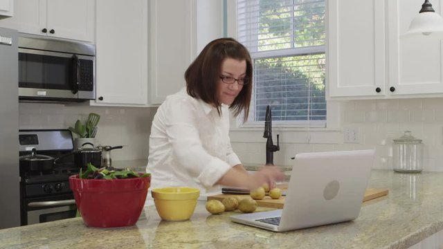 Woman using laptop and preparing food in large kitchen - 4K