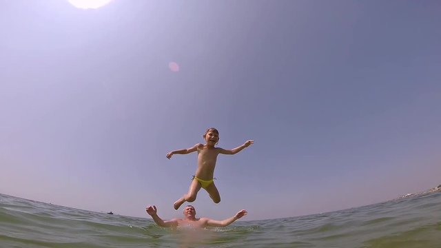 Dad throws up his daughter in the sea. Daughter dives and swims back to his father