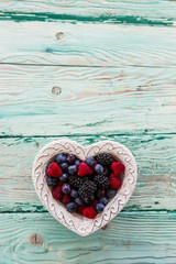 Forest fruits in a bowl in the shape of a heart on a wooden table with space for text.