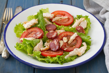 fresh salad with chicken and chourico on white dish on blue wooden background