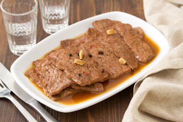fried meat with garlic and black pepper on white dish on brown wooden background