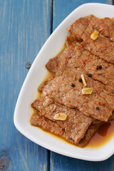 fried meat with garlic and black pepper on white dish on blue wooden background