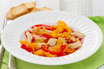 chicken with pepper and carrot on white plate and glass of water