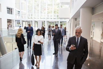 Businesspeople Using Technology In Busy Lobby Area Of Office