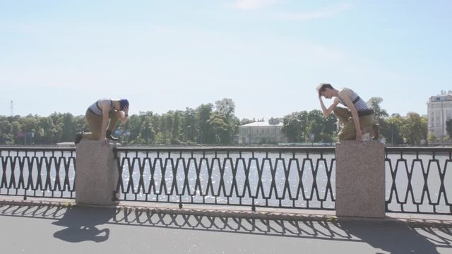 Two men in marine uniform sit on knee on postament at seafront, stand up together, weird. Surrealism. Water, summer sunny day