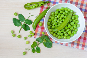 Fresh green peas in white ceramic bowl on wooden background. Top view.