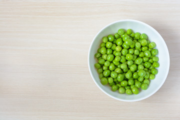 Fresh green peas in white ceramic bowl on wooden background. Top view.