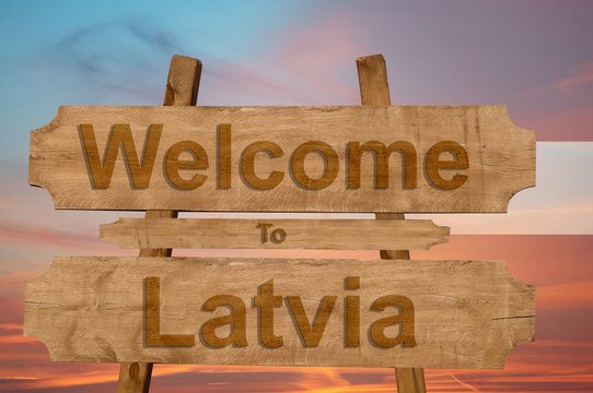 Welcome to Latvia sign on wood background with blending national flag