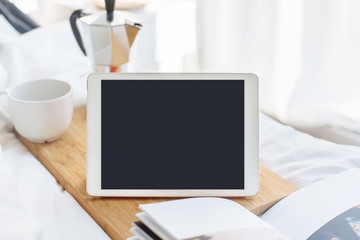 Breakfast in bed, Digital tablet with cup of coffee and coffee pot on background, Mock up of digital tablet with blank screen at the morning, blurred background, shallow DOF.