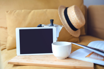 Digital tablet with cup of coffee, coffee pot, straw hat and magazine, Mock up of digital tablet with blank screen at the morning, blurred background, shallow DOF.