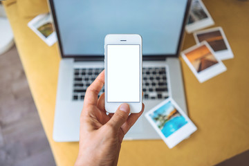 Closeup of female hand using smart phone with blank screen with an open laptop on background, hand holding modern smartphone, woman going on vacation, blurred background, shallow DOF.