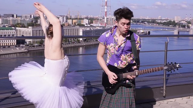 Man in scotland skirt play rock on electric guitar on seafront in sunny day. Girl dance in ballerina suit. Crazy people
