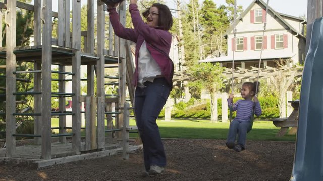Mother pushes her kids on playground swings - 4K