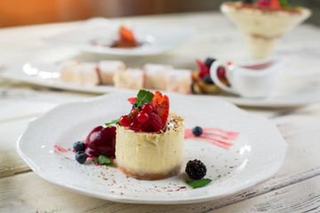 White plate with small cake. Ice cream and berries. Traditional recipe of cheesecake. Fresh dessert on cafe table.