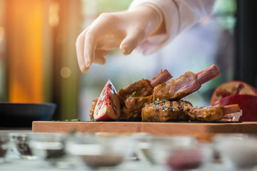 Hand near board with meat. Herbs and piece of pomegranate. Special recipe of veal ribs. Tasty and aromatic dish.
