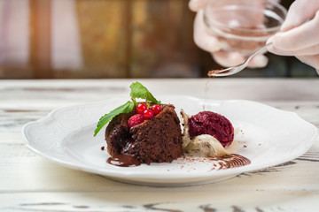 Chocolate crumbs fall on dessert. Hand with small spoon. Sponge cake and ice cream. Best sweet dish in cafe.