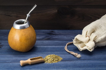 yerba mate with wooden spoon, gourd matero and linen bag on blue wooden table