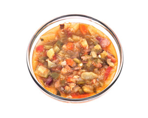 Vegetable soup with bacon in glass bowl separated on white background