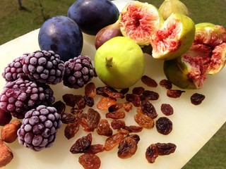 Photograph of plums, figs, blackberries, hazelnuts and raisins on white platter