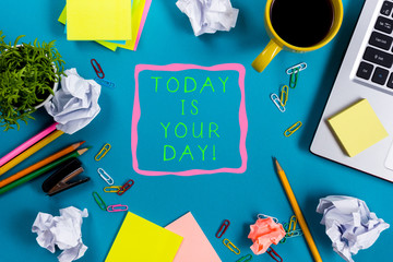 Today is your day. Office table desk with supplies, white blank note pad, cup, pen, pc, crumpled paper, flower on blue background. Top view