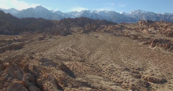 Sideways Desert Rock Snow Mountains / Aerial sideways flight of the desert with boulders, rocks, and snow covered mountains in the background.