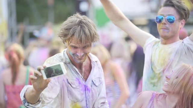 Excited friends covered in colorful powder at paint festival, posing for selfie