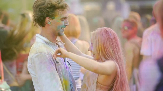 Happy couple hugging, flirting and dancing in crowd at outdoor color festival