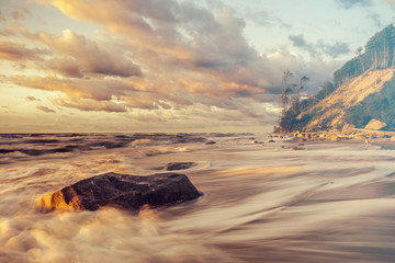Sea landscape at sunset, sandy beach and cliff,waves breaking on