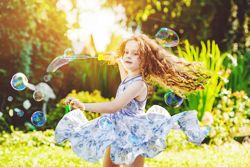 Curly girl in flying dress playing with soap Bubbles.