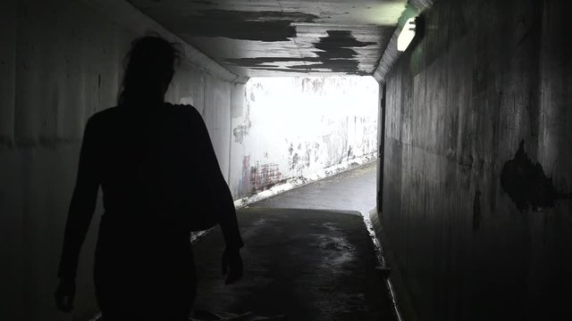 Silhouette of a man attacks  a young woman with a knife in a dark tunnel. Violence against women concept. Real people, copy space