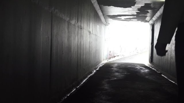 Silhouette of a man carry a knife follows a young woman in a dark tunnel. Violence against women concept. Real people, copy space