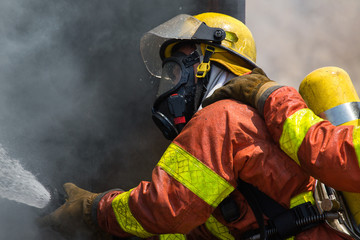 Fototapeta premium fireman in fire fighting suit spraying water to fire surround wi