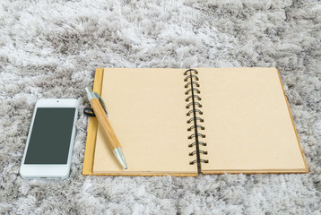 Closeup brown note book with blank space in page , brown pen and smart phone on gray fabric capet textured background in top view in work concept