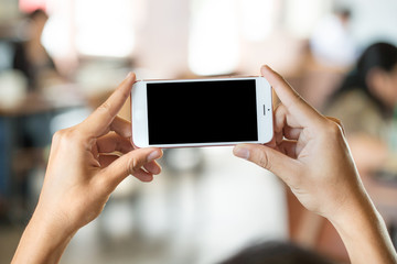 hand holding white  smartphone with blank screen in coffee shop