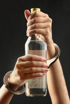 Bottle with alcohol drink in hands on a dark background. The concept of alcoholism