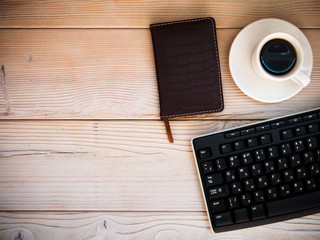 Office table with keyboard, notebook and cup of coffee. View from above