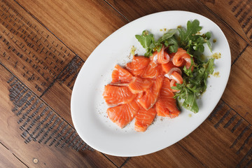 Smoked trout with greens on a white plate. Wooden background.