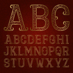 Golden ornamental letters with flourishes on red patterned background. Vintage decorative font. Isolated latin alphabet.
