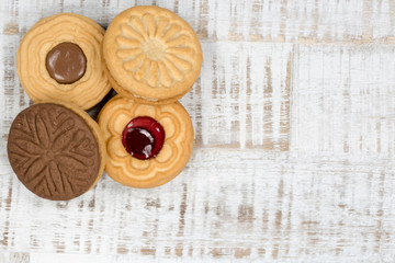 Vier runde Kekse, mit Schokolade und Marmelade, auf einem hellen Holztisch