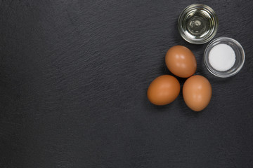Drei braune Eier, eine Schale Öl und Salz auf einer Schieferplatte in der rechten oberen Ecke
