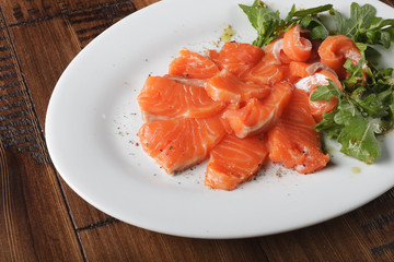 Smoked trout with greens on a white plate. Wooden background.